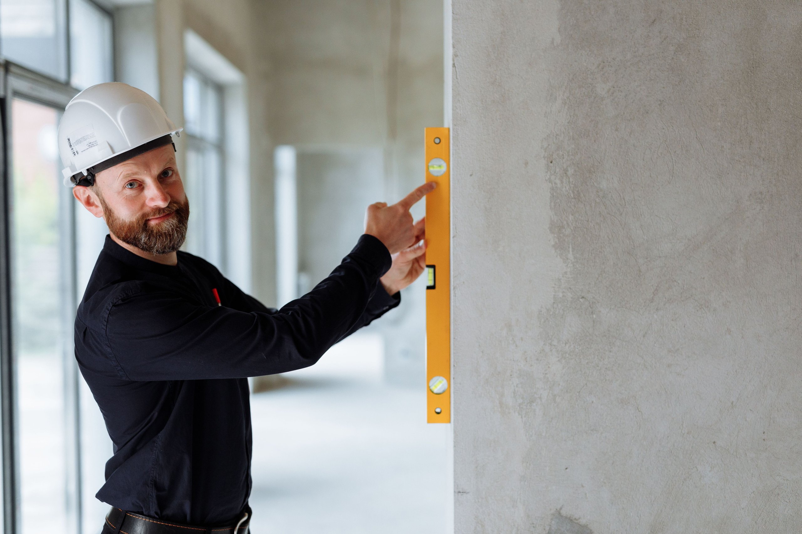 Construction worker in a hard hat checking a concrete wall with a level